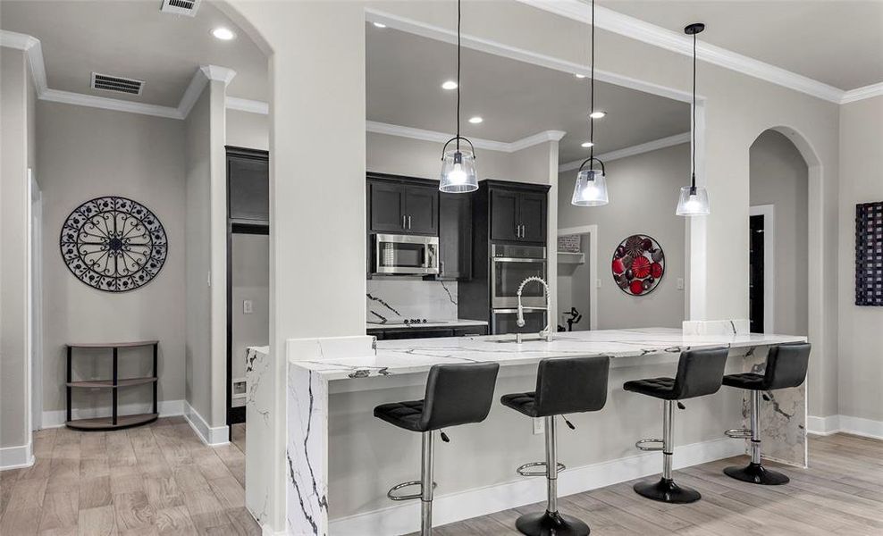 Kitchen featuring arched walkways, light stone countertops, light wood-style flooring, a breakfast bar area, and crown molding