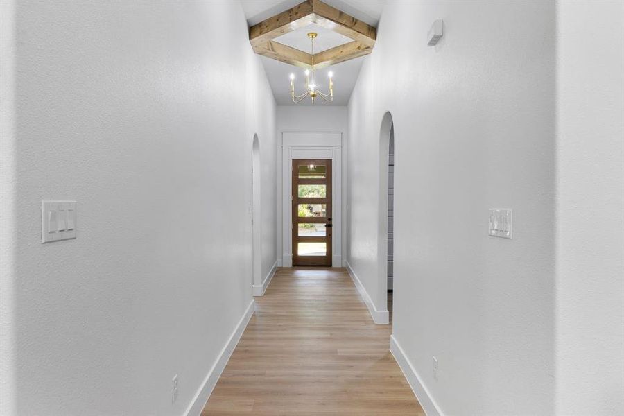 Corridor with a chandelier, light hardwood / wood-style flooring, and vaulted ceiling with beams