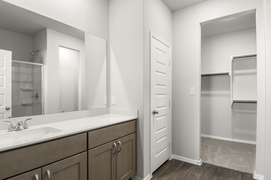 Image of a primary bathroom with a double white vanity, brown cabinets, a walk-in closet and a large mirror