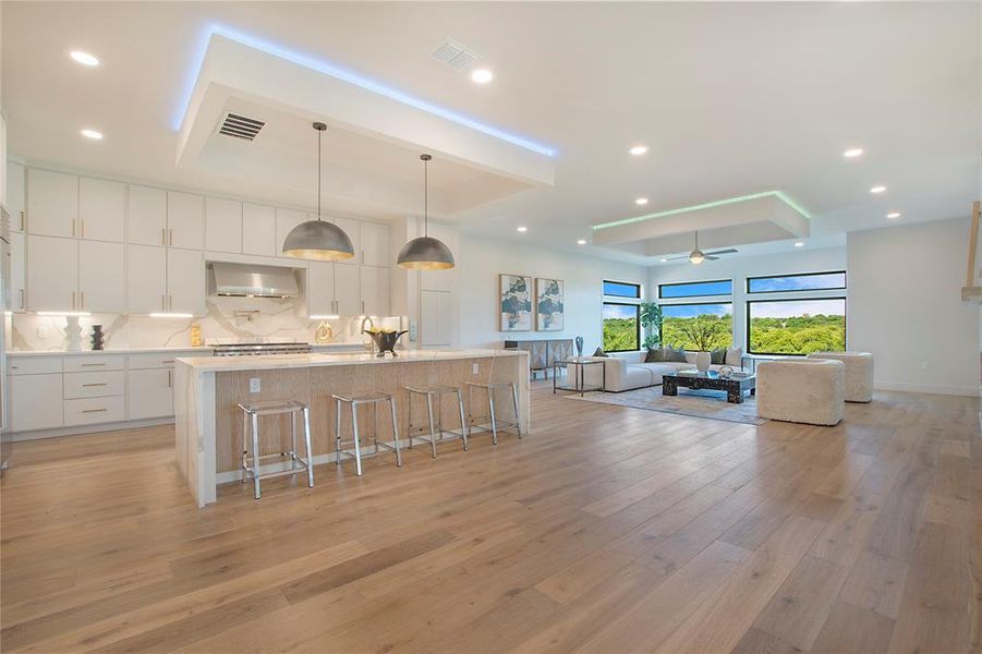 Kitchen with light hardwood / wood-style flooring, a center island with sink, wall chimney range hood, hanging light fixtures, and white cabinetry