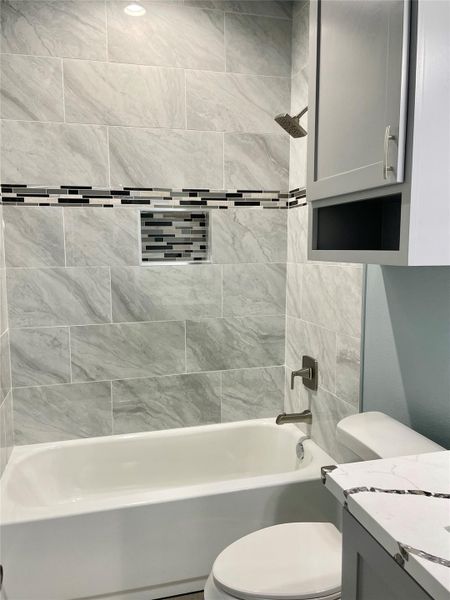 Modern bath features a tub with showerhead, complemented by sleek gray tile and practical cabinet storage.