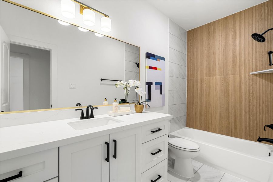 First floor bathroom features a sleek white vanity with black fixtures, a large mirror with stylish lighting, and a bathtub with a wood-accented wall.