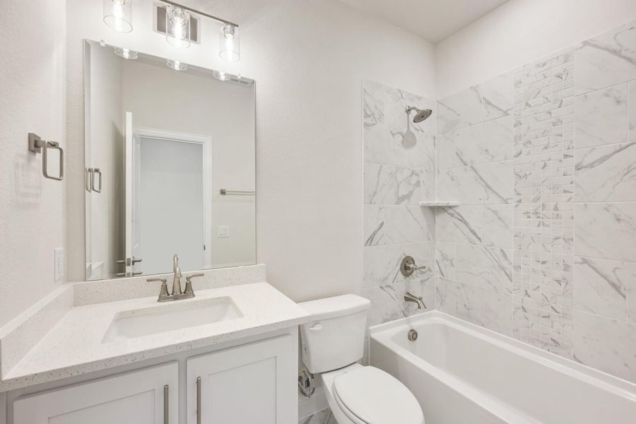 Bathroom with white vanity, quartz countertop, and tub-shower combo with marble-look tile surround