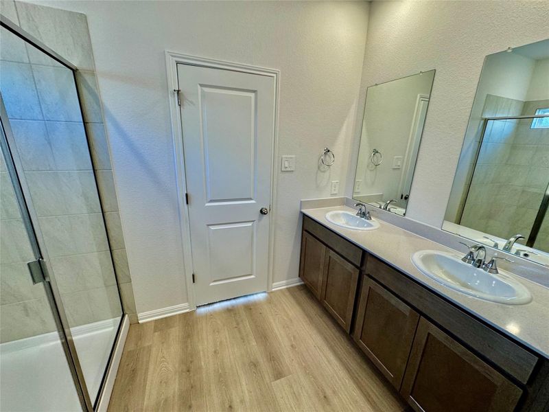 Full bath featuring a shower stall, double vanity, light wood-type flooring, and a textured wall