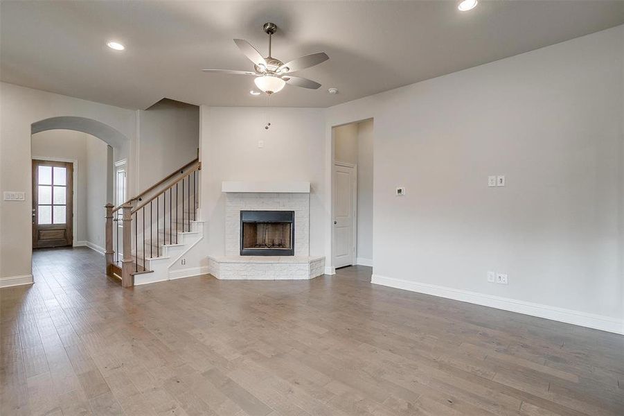 Unfurnished living room with wood-type flooring, a brick fireplace, and ceiling fan