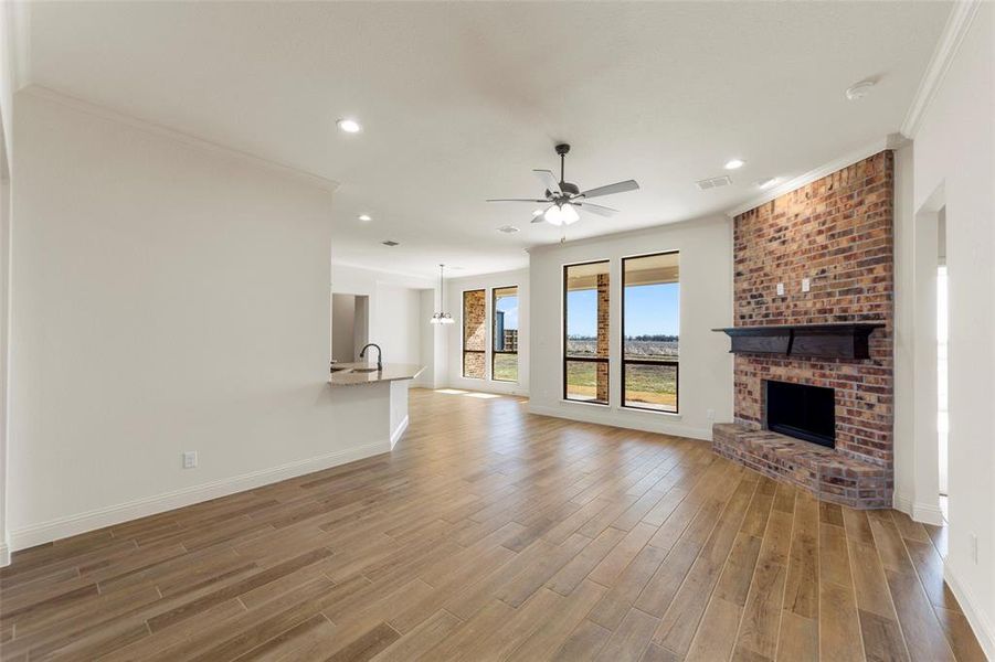 Unfurnished living room featuring light wood finished floors, ceiling fan, recessed lighting, a brick fireplace, and ornamental molding Unfurnished living room featuring light wood finished floors, ceiling fan, recessed lighting, a brick fireplace, and ornamental molding