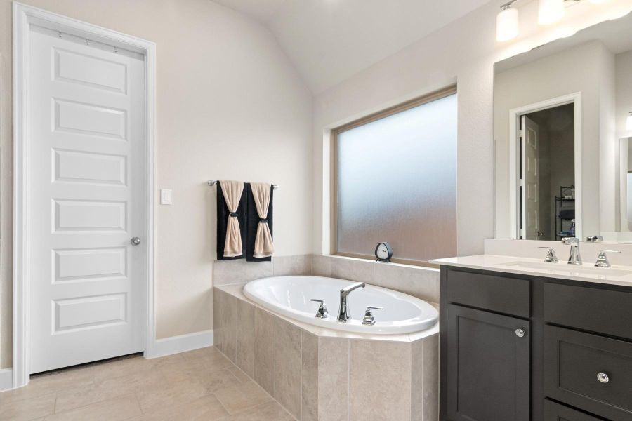 This modern bathroom features a sleek soaking tub with a tile surround, a spacious double vanity with ample storage, and a large frosted window for natural light. Neutral tones create a relaxing atmosphere.