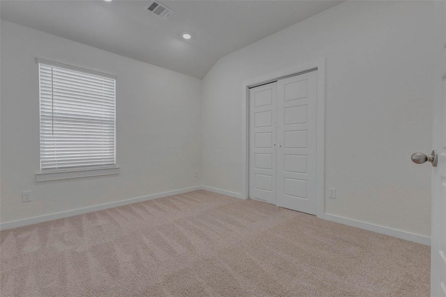 This secondary bedroom offers a clean, neutral canvas with plush carpet, recessed lighting, and a large window that welcomes natural light. Double-door closets add functionality and style, while the soft color palette makes this space ideal for guests, children, or a home office setup.