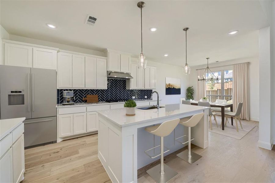 Virtually Staged Photo - Kitchen with light hardwood / wood-style flooring, tasteful backsplash, a center island with sink, sink, and stainless steel fridge with ice dispenser