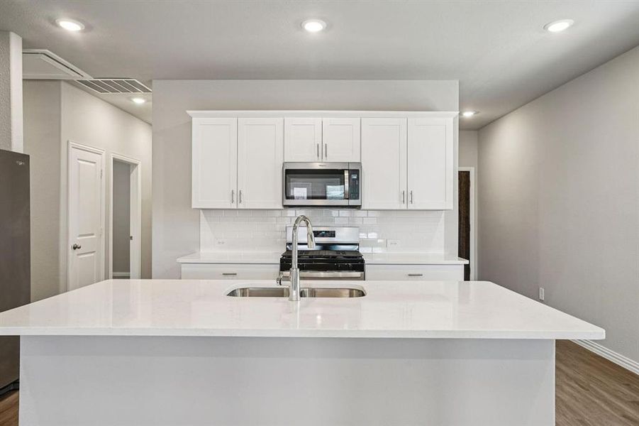 Kitchen with white cabinets, stainless steel appliances, dark wood-type flooring, light stone countertops, and a center island with sink