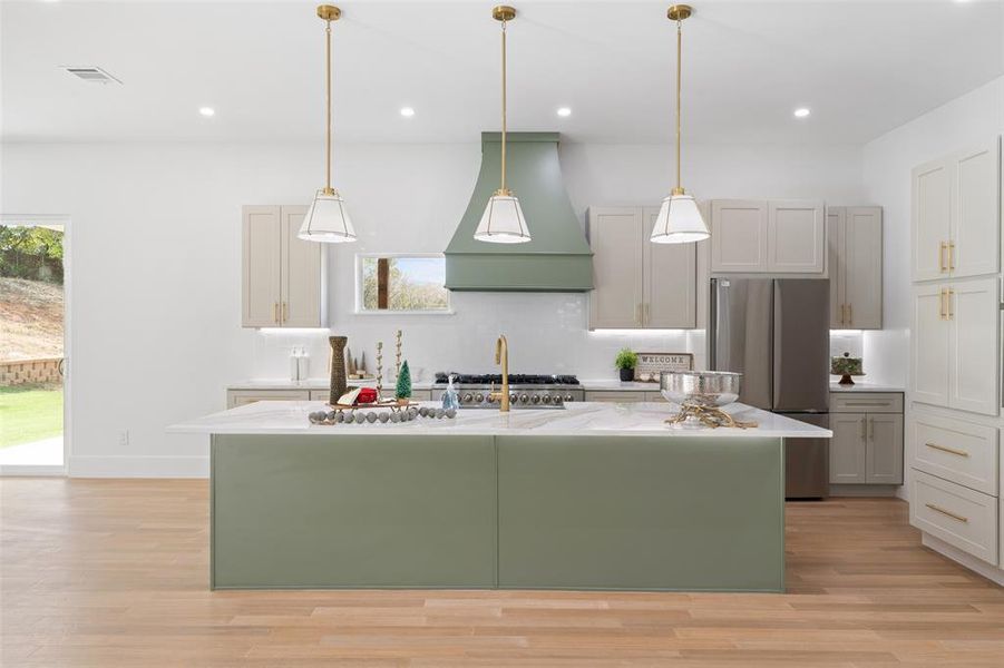 Kitchen featuring green cabinets, an island with sink, freestanding refrigerator, premium range hood, and recessed lighting