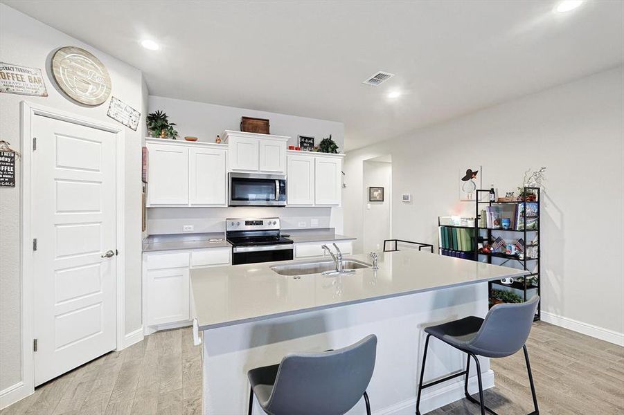 Kitchen with a kitchen island with sink, stainless steel appliances, a sink, white cabinetry, and light countertops