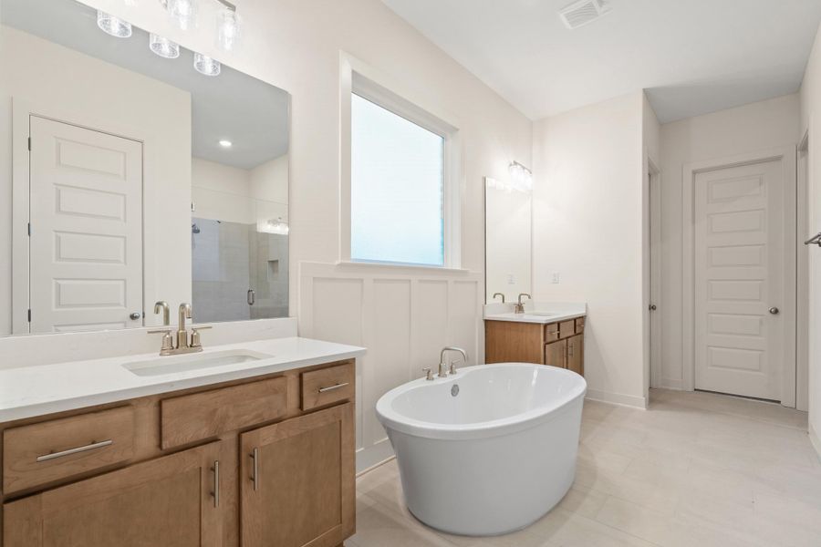 Bathroom featuring a freestanding oval tub, two separate vanity sinks with light wood cabinetry and light countertops, a large rectangular window, and light wood-finish flooring Bathroom featuring a freestanding oval tub, two separate vanity sinks with light wood cabinetry and light countertops, a large rectangular window, and light wood-finish flooring