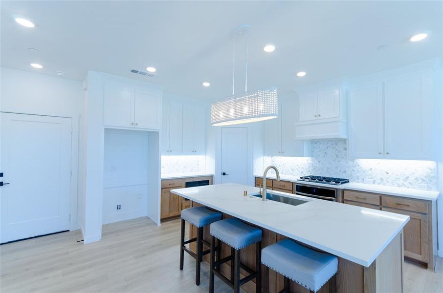 Two tone kitchen featuring a kitchen bar, two tone cabinetry, backsplash, light wood-type flooring, and an island with sink