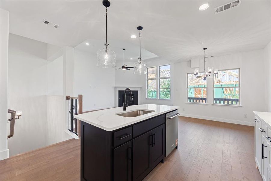 Kitchen featuring dark cabinets, light wood-style flooring, decorative light fixtures, a kitchen island with sink, and light stone counters Kitchen featuring dark cabinets, light wood-style flooring, decorative light fixtures, a kitchen island with sink, and light stone counters