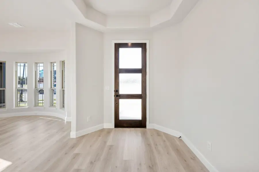 Entryway with dark wood glass-panel front door, tray ceiling, and light hardwood floors