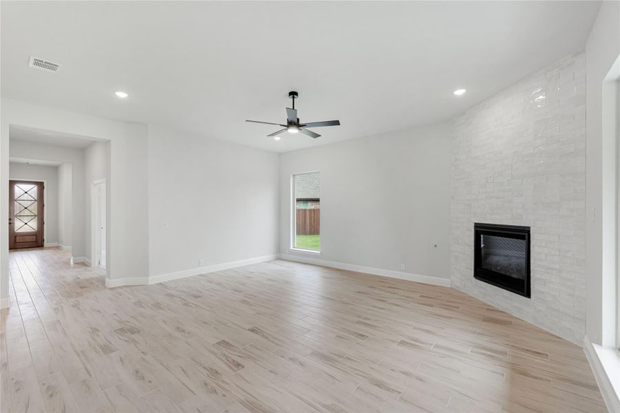 Open living room with light wood floors, ceiling fan, and tile-surround fireplace on accent wall Open living room with light wood floors, ceiling fan, and tile-surround fireplace on accent wall