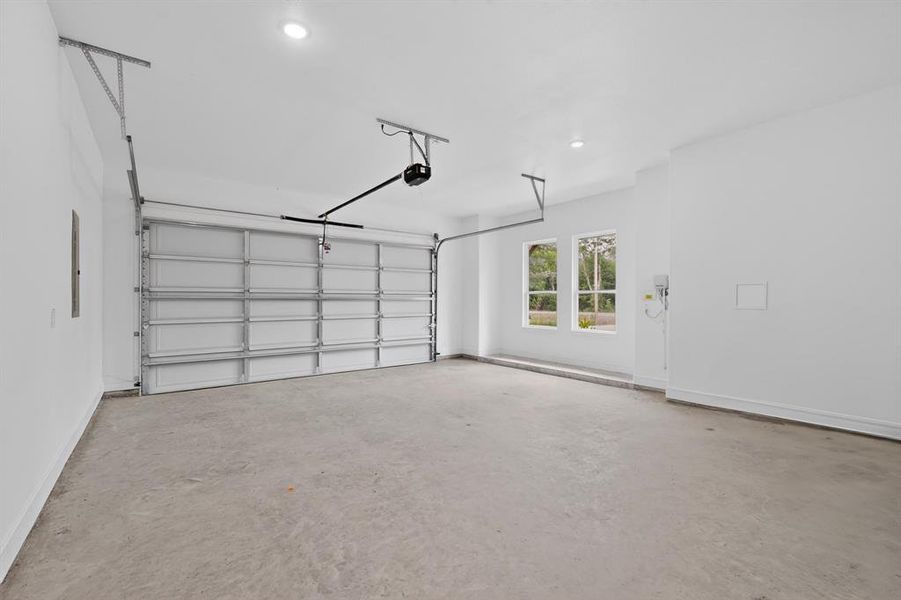 Spacious garage featuring a concrete floor, bright white walls, and a large overhead garage door with an automatic opener