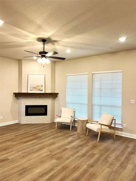 Living area featuring wood finished floors, a textured ceiling, baseboards, a glass covered fireplace, and a ceiling fan Living area featuring wood finished floors, a textured ceiling, baseboards, a glass covered fireplace, and a ceiling fan