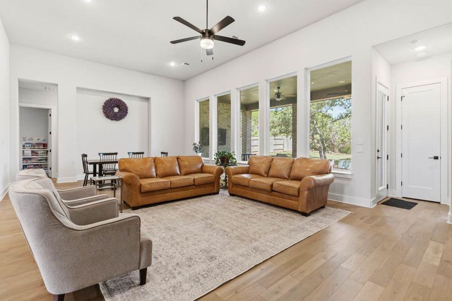 A spacious living room features large windows and light wood flooring, offering a serene view of the outdoors.