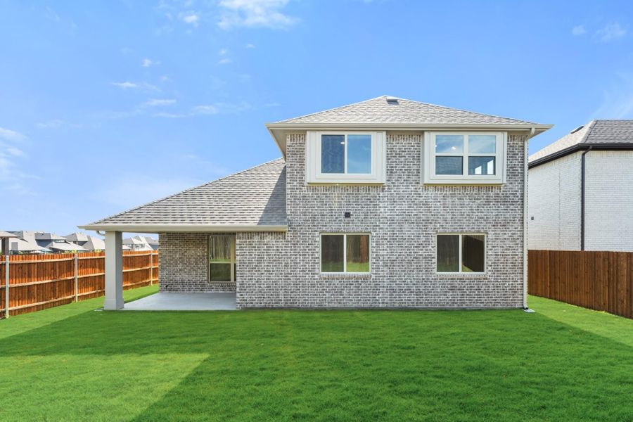 Two-story brick home rear view with covered patio, green lawn, and wood privacy fence