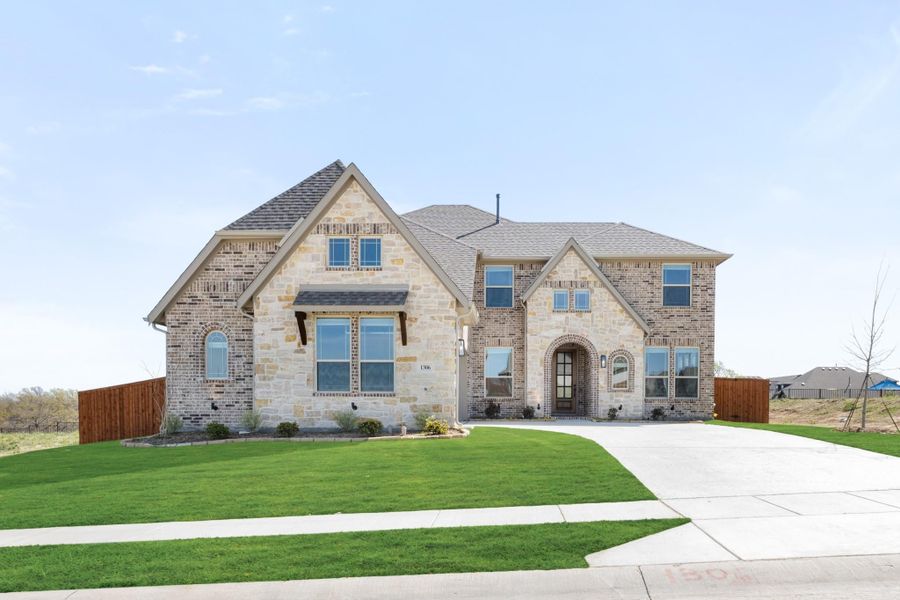 Two-story brick and stone home with arched entry, large windows, and manicured front lawn