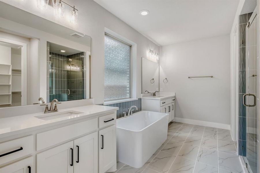 Bathroom featuring a stall shower, a freestanding bath, two vanities, light marble finish flooring, and a spacious closet