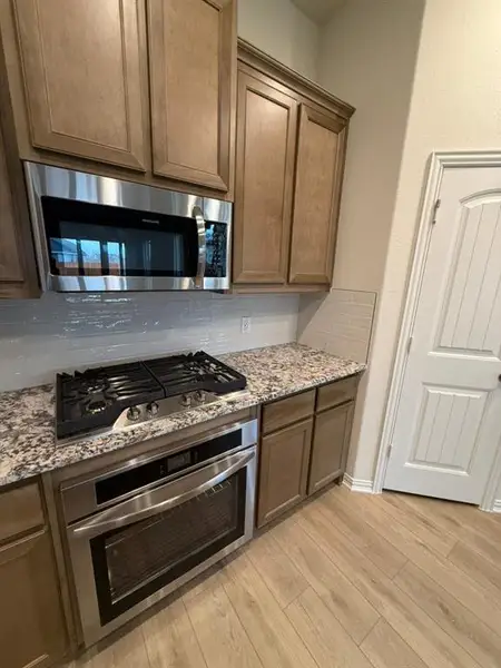 Kitchen featuring appliances with stainless steel finishes, light stone countertops, light wood-style floors, and backsplash Kitchen featuring appliances with stainless steel finishes, light stone countertops, light wood-style floors, and backsplash