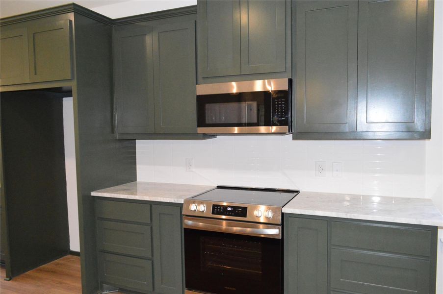 Kitchen featuring appliances with stainless steel finishes, light stone countertops, decorative backsplash, and wood finished floors Kitchen featuring appliances with stainless steel finishes, light stone countertops, decorative backsplash, and wood finished floors