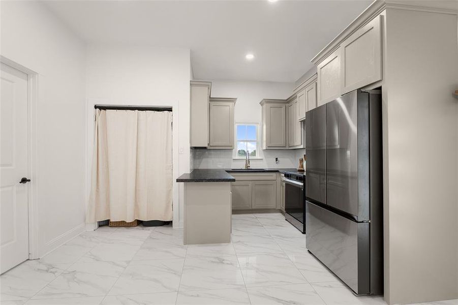 Kitchen with appliances with stainless steel finishes, light marble finish flooring, dark stone countertops, recessed lighting, and tasteful backsplash