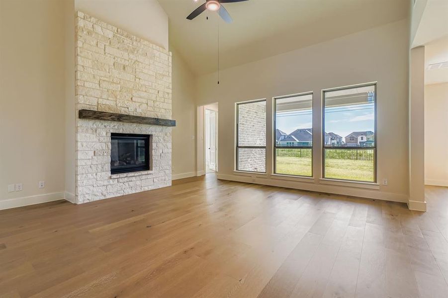 Unfurnished living room featuring a ceiling fan, high vaulted ceiling, wood finished floors, a fireplace, and a residential view