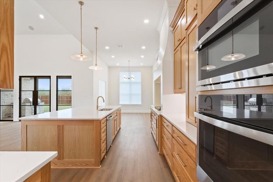 Kitchen with stainless steel appliances, light wood-style floors, light brown cabinetry, decorative light fixtures, and a large island