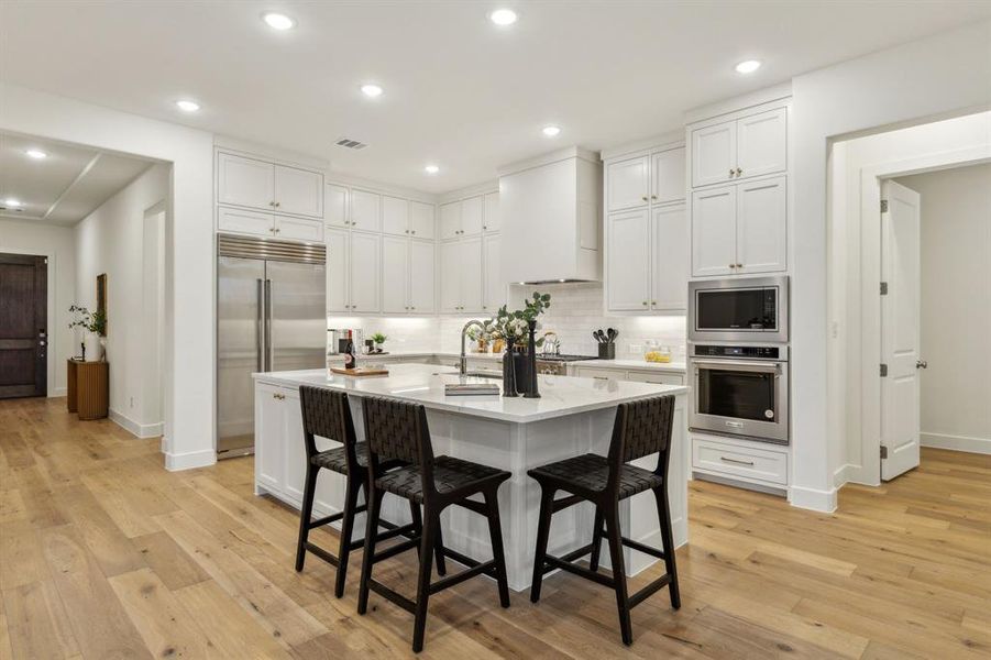 Kitchen featuring built in appliances, white cabinetry, and custom range hood