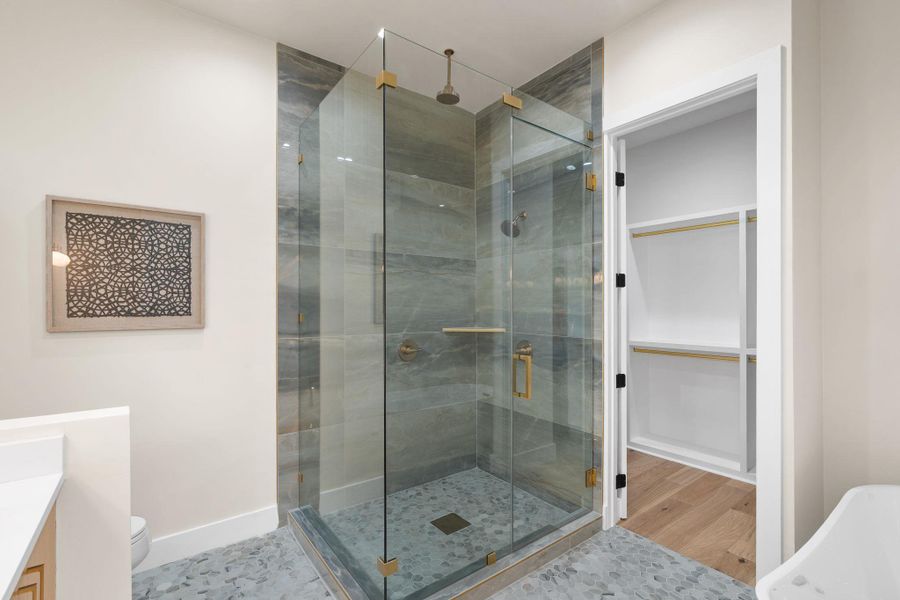 Glass-enclosed shower with stone tile walls, rainfall showerhead, and gold-finish hardware