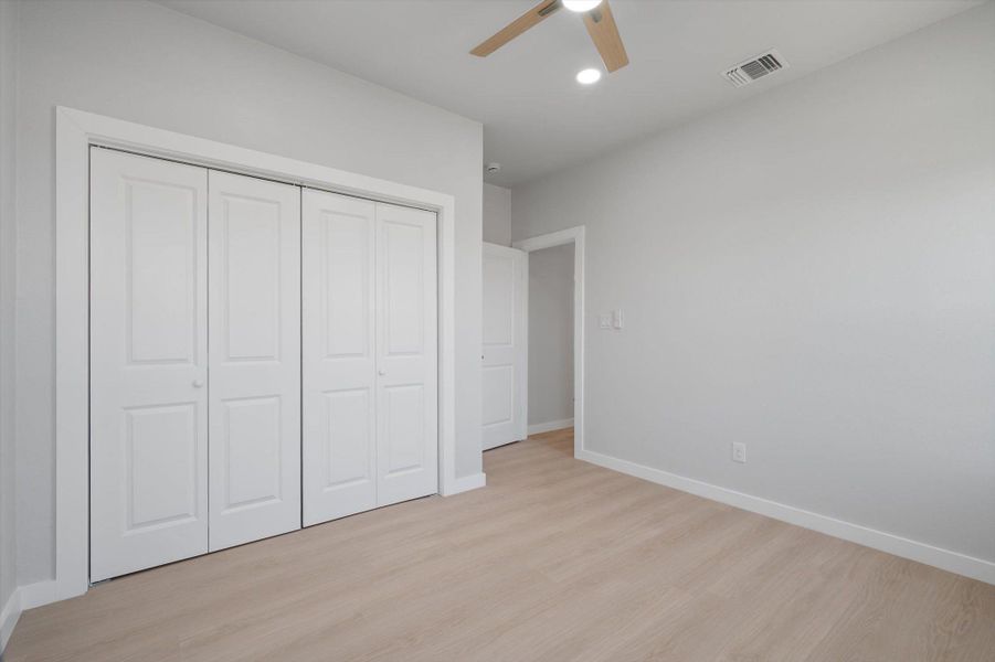 Laminate flooring and bright white walls create a serene, open atmosphere in this well-appointed bedroom.