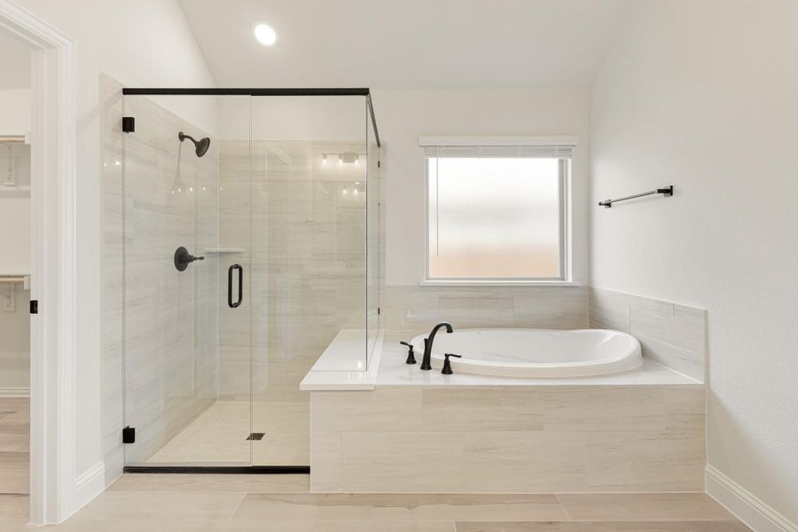 Master bathroom with glass-enclosed walk-in shower, soaking tub, and light tile flooring with black fixtures
