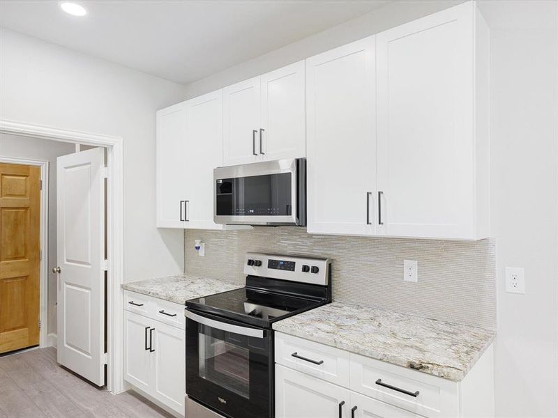 Kitchen featuring stainless steel appliances, white cabinetry, light stone countertops, decorative backsplash, and recessed lighting