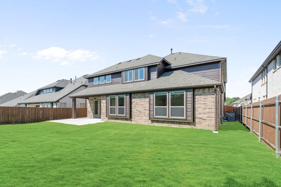 Two-story brick home rear view with large green backyard, covered patio, and wood privacy fence