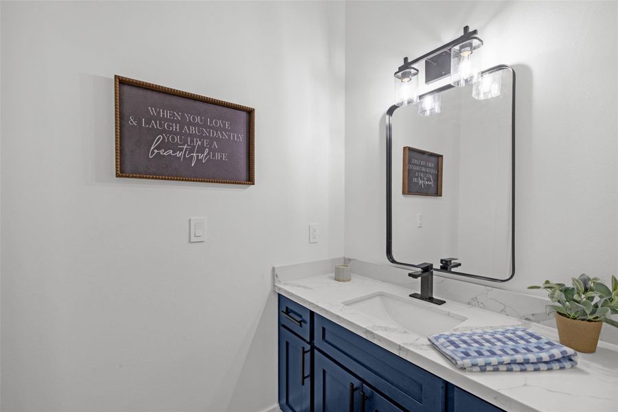 Contemporary bathroom with a sleek black-framed mirror and light fixture. It has a stylish white countertop with an under-mount sink and dark blue cabinetry. Contemporary bathroom with a sleek black-framed mirror and light fixture. It has a stylish white countertop with an under-mount sink and dark blue cabinetry.