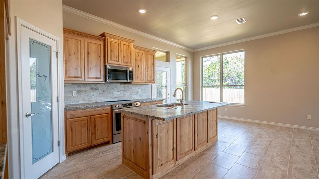 Kitchen featuring light stone counters, stainless steel appliances, a center island with sink, decorative backsplash, and crown molding