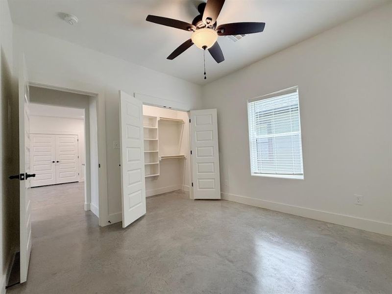 Unfurnished bedroom with finished concrete floors, a walk in closet, and ceiling fan Unfurnished bedroom with finished concrete floors, a walk in closet, and ceiling fan