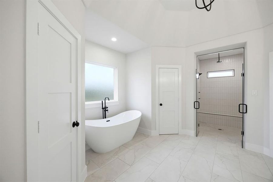 Freestanding soaking tub with a matte black faucet, glass-enclosed shower with tile surround and bench, white paneled doors, and large format floor tiles