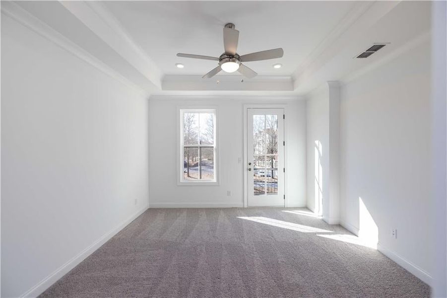 The primary bedroom has lush carpet, a tray ceiling and access to another small balcony.