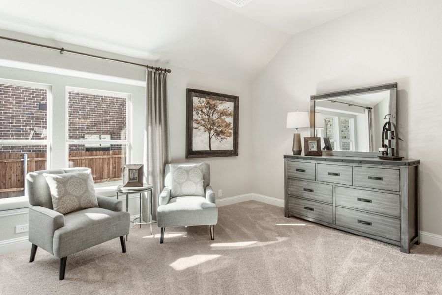 Bedroom sitting area with two gray chairs, dresser with mirror, and vaulted ceiling over carpet flooring