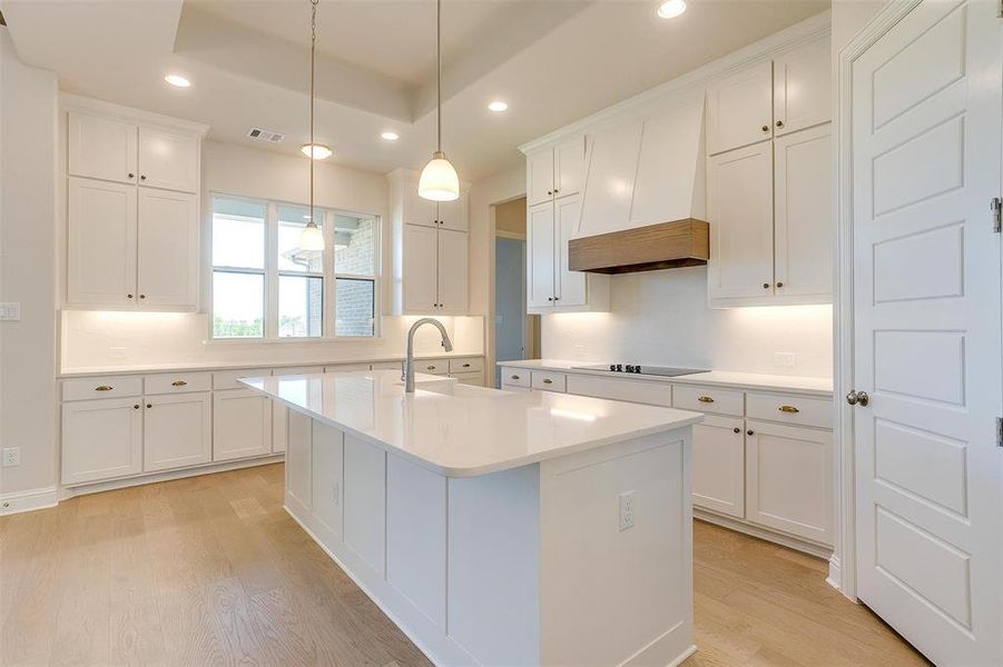 Kitchen featuring premium range hood, white cabinets, light wood-type flooring, sink, and a center island with sink