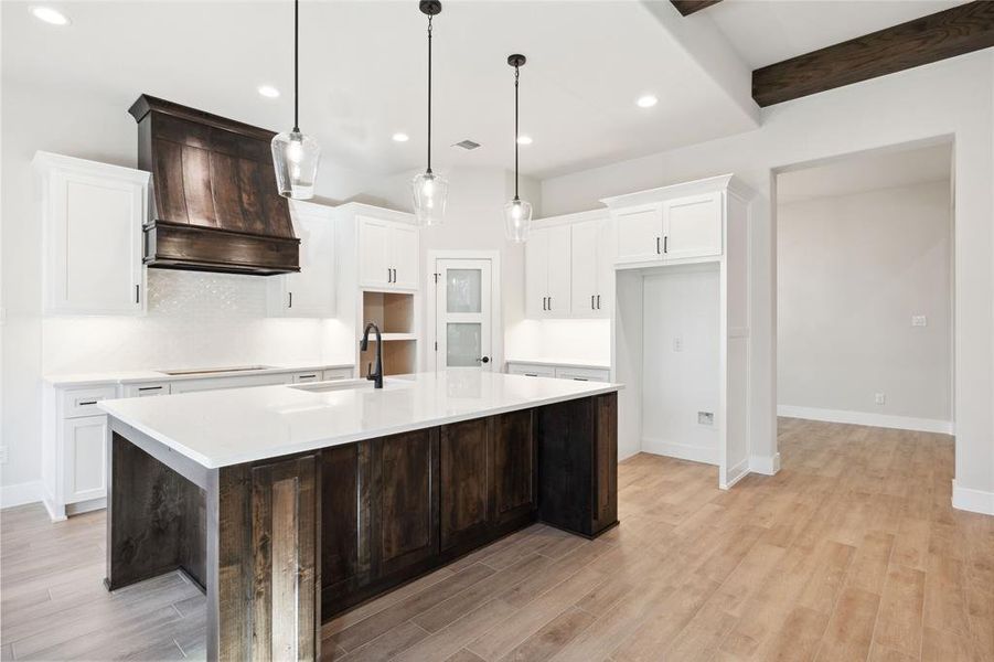 Kitchen featuring sink, beamed ceiling, premium range hood, pendant lighting, and a kitchen island with sink