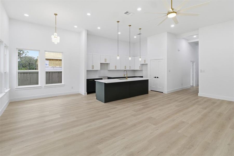 Kitchen featuring dark cabinetry, open floor plan, white cabinetry, a towering ceiling, and a kitchen island with sink