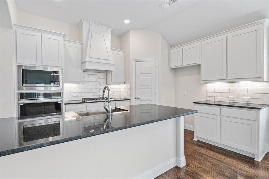 Kitchen with white cabinets, backsplash, dark stone countertops, stainless steel appliances, and dark wood finished floors Kitchen with white cabinets, backsplash, dark stone countertops, stainless steel appliances, and dark wood finished floors