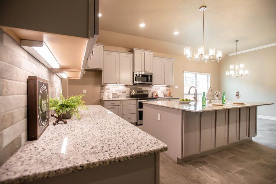 Kitchen featuring a kitchen island with sink, backsplash, appliances with stainless steel finishes, light stone countertops, and a chandelier