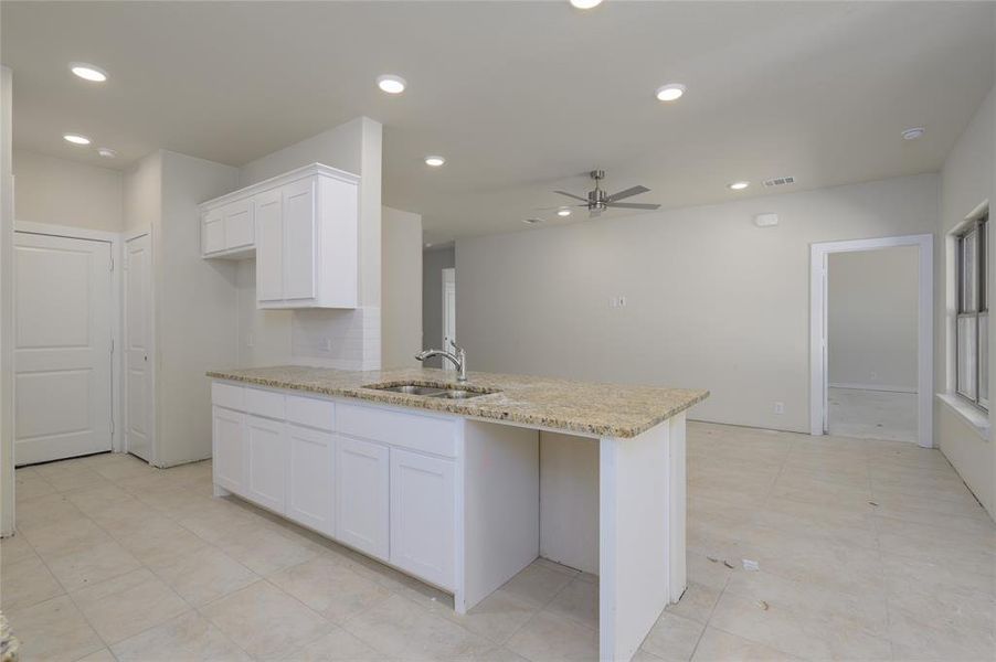 Kitchen featuring light stone countertops, kitchen peninsula, ceiling fan, sink, and white cabinets